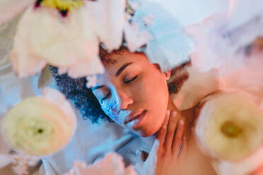 Young woman with eyes closed lying behind glass surface under neon lights - YTF01699