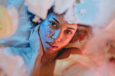 Beautiful woman lying below glass surface with flowers under neon lights - YTF01700