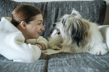 Smiling woman lying face to face with dog on sofa at home - OSF02380