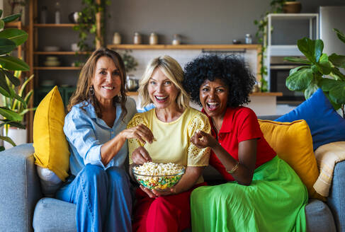 Fröhliche Freunde sitzen auf dem Sofa und teilen sich Popcorn zu Hause - OIPF03878