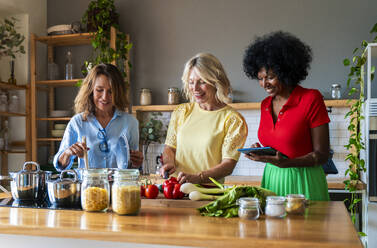 Happy friends cooking food together in kitchen at home - OIPF03902