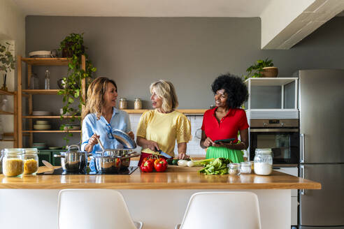 Gemischtrassige Freunde unterhalten sich und kochen zusammen in der Küche zu Hause - OIPF03904