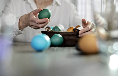 Woman keeping green egg in easter basket at home - MBLF00255