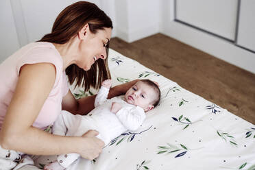 Happy mother playing with baby girl on bed at home - EBBF08409