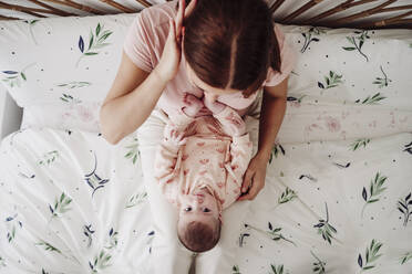 Mother sitting on bed with baby girl in bedroom at home - EBBF08418