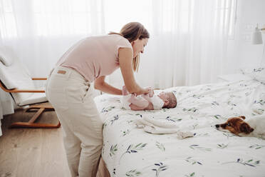 Frau wechselt die Kleidung ihrer Tochter auf dem Bett zu Hause - EBBF08419