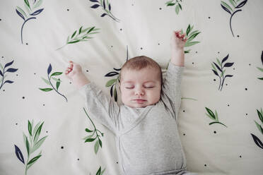 Cute baby girl stretching arms lying in bed at home - EBBF08434