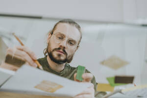 Fokussierter Möbeldesigner bei der Arbeit am Schreibtisch, gesehen durch Glas im Büro - YTF01715