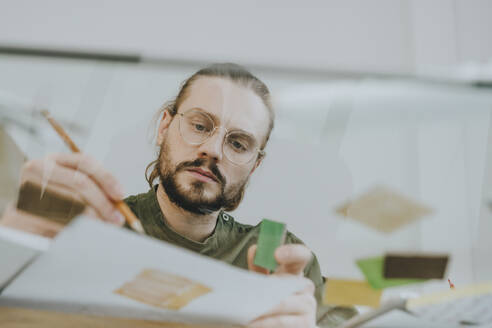 Focused furniture designer working at desk seen through glass at office - YTF01715