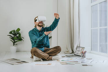 Smiling interior designer wearing virtual reality simulator and sitting on office floor - YTF01734