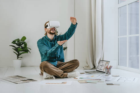 Lächelnder Innenarchitekt, der einen Virtual-Reality-Simulator trägt und auf dem Büroboden sitzt - YTF01734