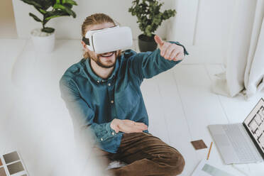 Smiling interior designer wearing VR glasses and gesturing at office - YTF01736