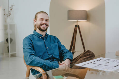 Happy interior designer sitting on chair at office - YTF01744