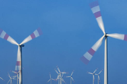 Wind farm turbines spinning against blue sky - JATF01386