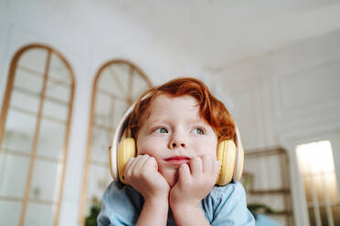 Rothaariger Junge hört zu Hause Musik über drahtlose Kopfhörer - MDOF01795