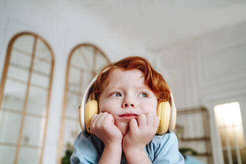 Redhead boy listening to music through wireless headphones at home - MDOF01795