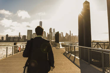 Businessman walking on bridge at sunset in city - UUF31135