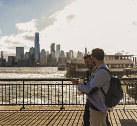 Young business colleagues sharing smart phone and walking at promenade in city - UUF31137