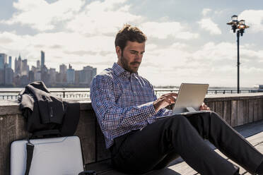 Businessman using tablet PC sitting on bench in city - UUF31148