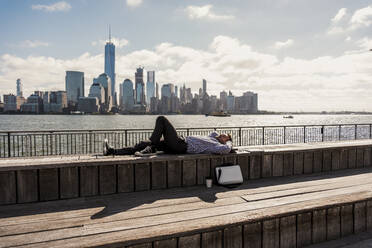 Sorgloser Geschäftsmann macht ein Nickerchen auf einer Bank mit Skyline im Hintergrund in der Stadt - UUF31149