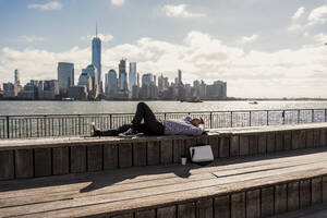 Carefree businessman taking nap lying on bench with skyline in background in city - UUF31149