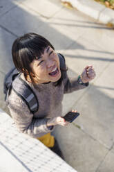 Fröhliche Frau beim Spaziergang mit Smartphone - IKF01682