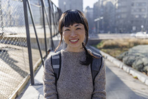 Smiling mature woman standing on footpath - IKF01687