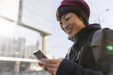 Lächelnde reife Frau, die ein Smartphone an einem sonnigen Tag benutzt - IKF01715