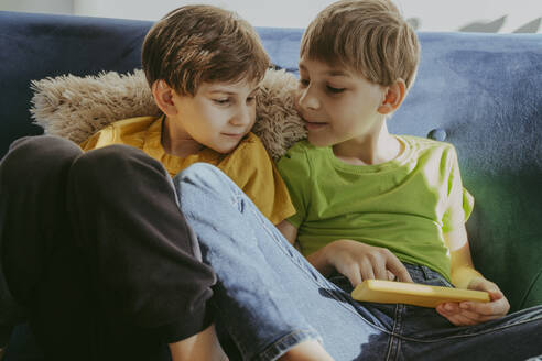Geschwister teilen sich ein Smartphone, während sie zu Hause auf dem Sofa sitzen - OSF02382