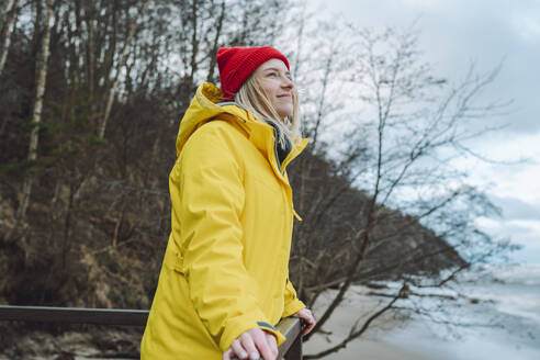 Smiling woman wearing winter jacket at beach - OLRF00134