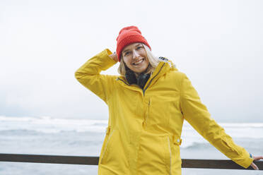 Happy young woman wearing winter jacket by sea - OLRF00136
