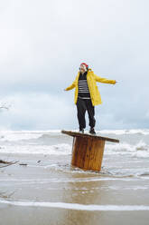 Carefree woman standing on wooden spool at beach - OLRF00137