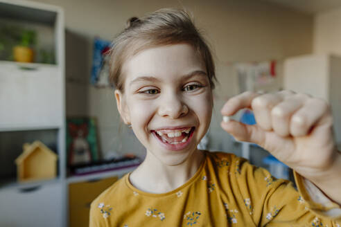 Cheerful girl holding broken tooth at home - YTF01747
