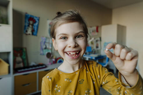 Happy girl holding broken tooth at home - YTF01748