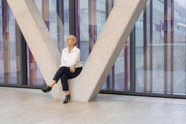 Ältere Geschäftsfrau sitzt inmitten einer architektonischen Säule - JOSEF23350