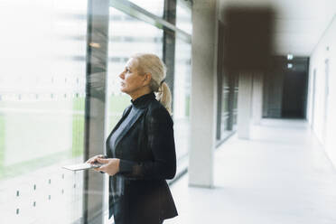 Senior businesswoman holding tablet PC in corridor - JOSEF23384