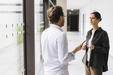 Young businesswoman talking to colleague standing in corridor - JOSEF23397