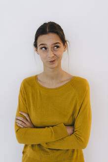 Young businesswoman standing with arms crossed and making face in front of white wall - JOSEF23428