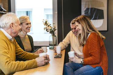 Happy friends sitting with coffee cup and enjoying retirement together - PBTF00441