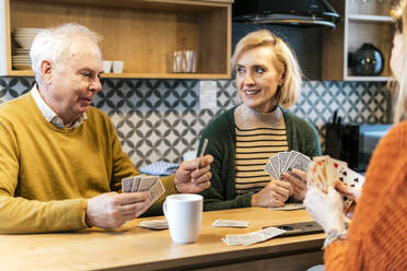 Happy friends enjoying and playing cards at home - PBTF00457