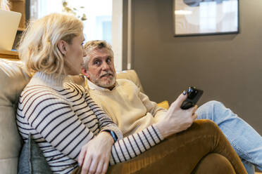 Man talking to woman sitting on sofa at home - PBTF00468
