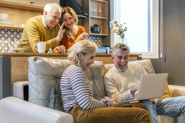 Happy friends talking on video call in living room at home - PBTF00469