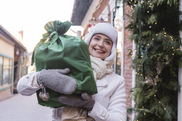 Glückliche Frau mit grüner Geschenktüte auf der Straße in der Weihnachtszeit - OSF02385