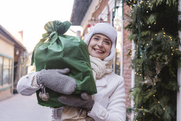 Happy woman carrying green gift bag at street in Christmas - OSF02385