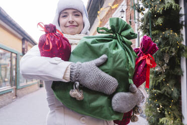 Smiling woman carrying gift bags at street in Christmas - OSF02386