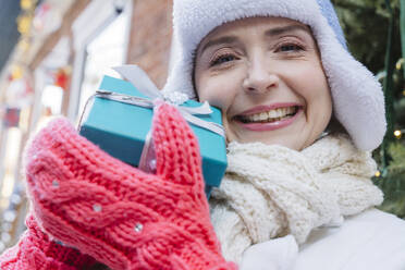 Happy woman wearing warm clothes and showing gift box - OSF02389