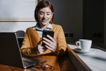 Freelancer using smart phone and sitting with laptop in cafe - EBBF08436