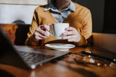 Freelancer holding coffee cup and sitting at table - EBBF08437