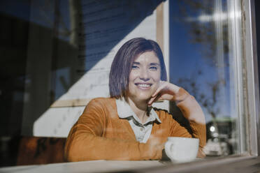 Lächelnde Frau mit Kaffeetasse im Café sitzend - EBBF08459