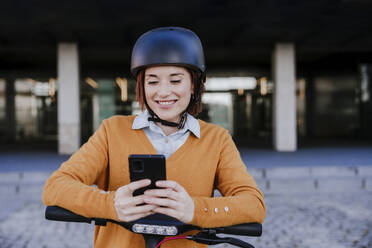 Lächelnde Frau mit Smartphone in der Nähe eines Gebäudes - EBBF08471